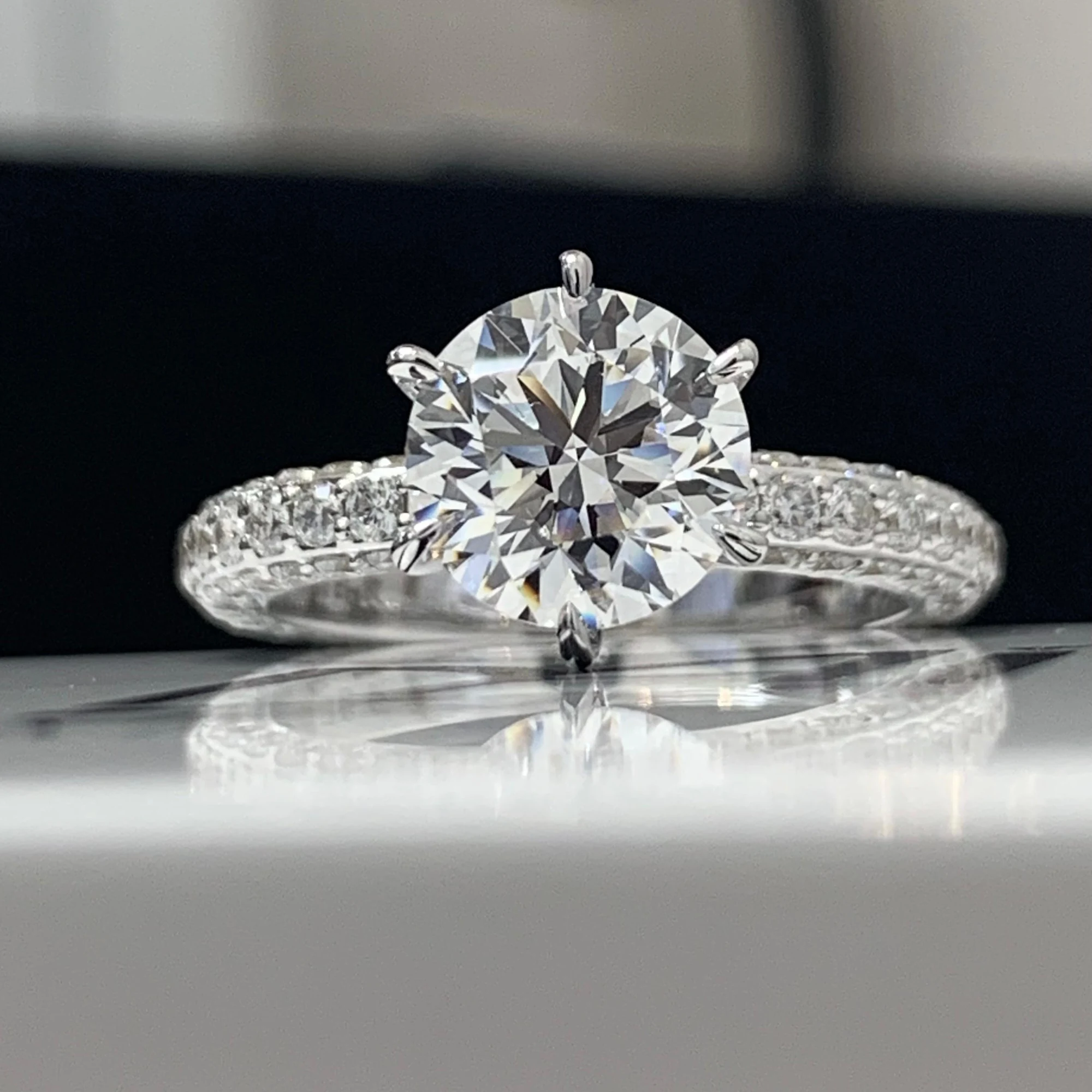 Round diamond solitaire ring with a diamond-set band on a reflective surface